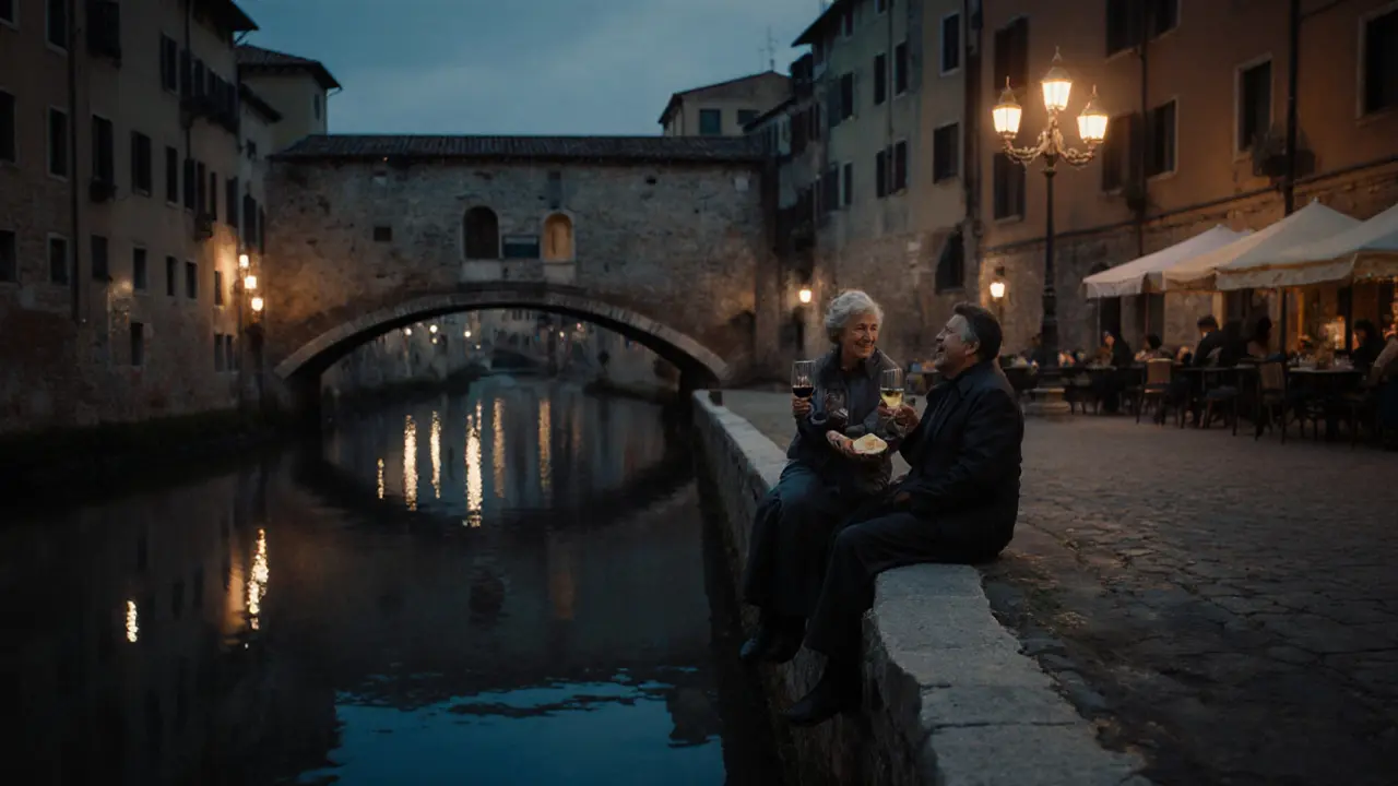 Two people sit by the Navigli canal at night sharing wine and cheese under soft lantern light.