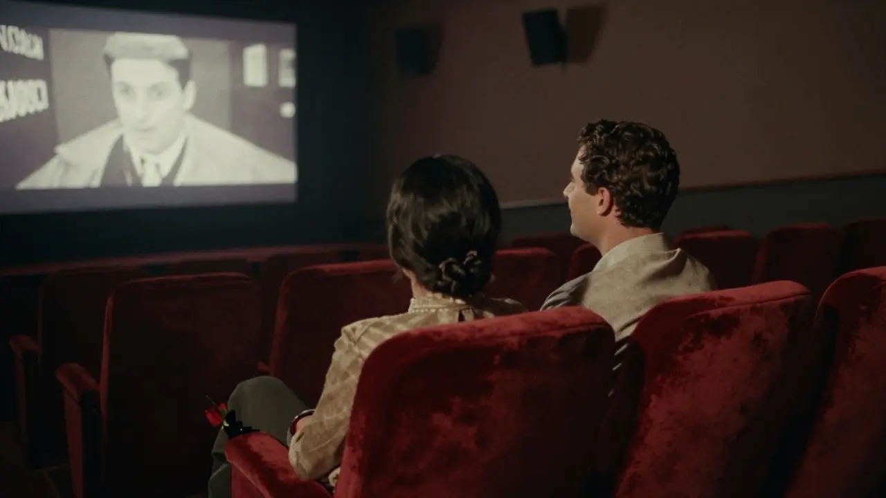 A couple watching a silent film in a vintage theater, a rose resting on the seat between them.